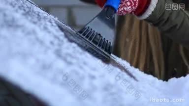 冬季早晨，用刮冰器从汽车挡风玻璃上刮冰的妇女的手特写聚焦在刮冰器上